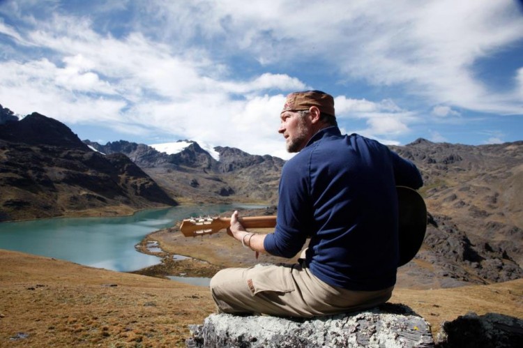 Survivorman playing a guitar in the wilderness.